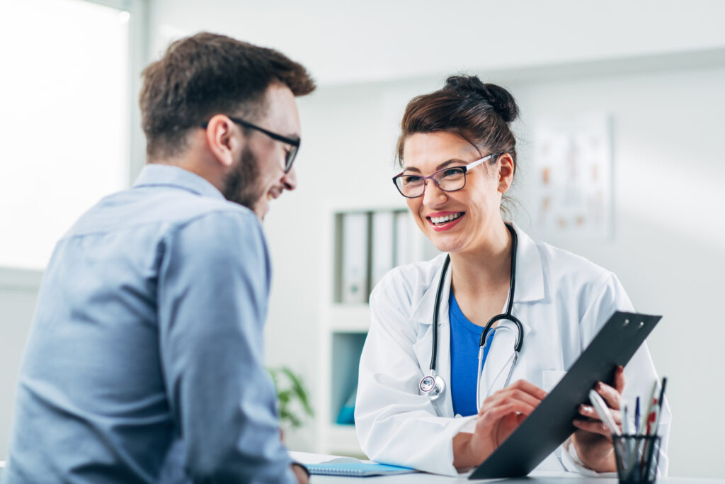 Doctor smiling wearing white coat and stethoscope talking with male employee